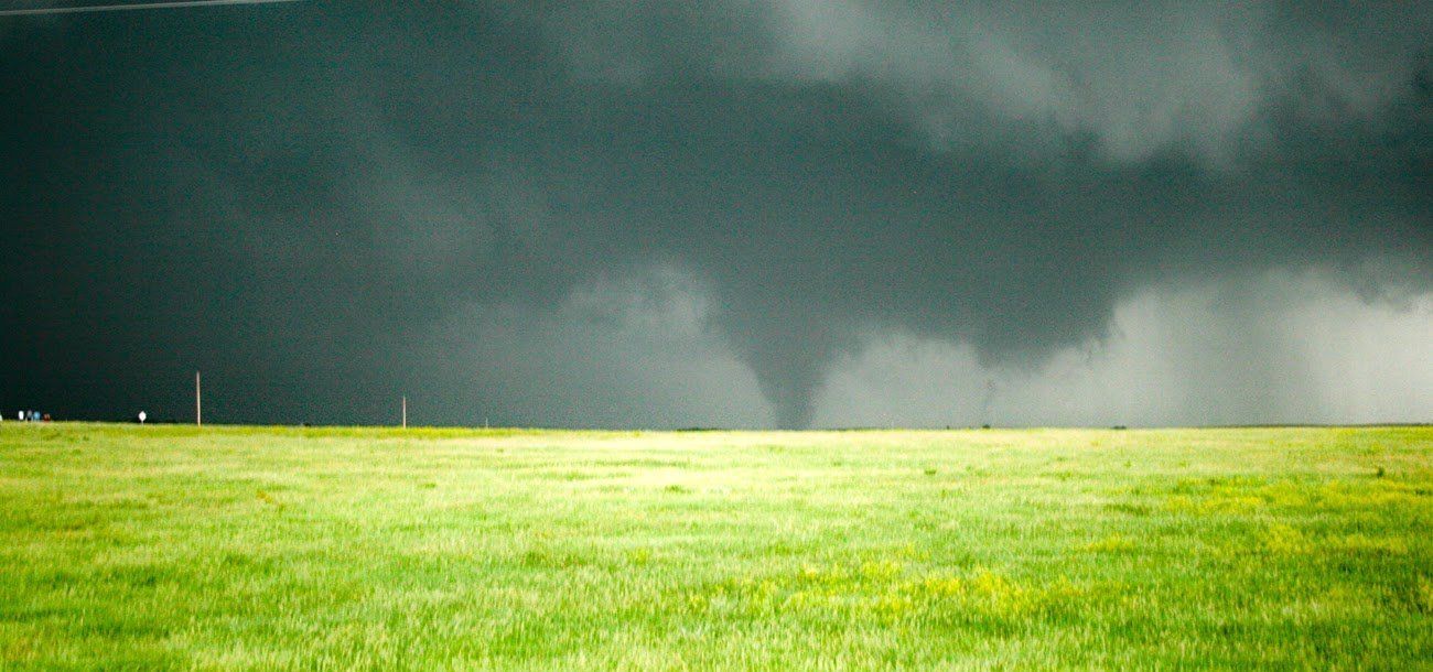 A tornado is moving through a grassy field with a dark sky in the background.