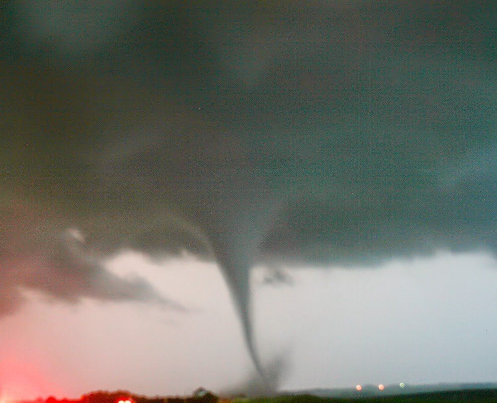 A large tornado is moving through a field at night