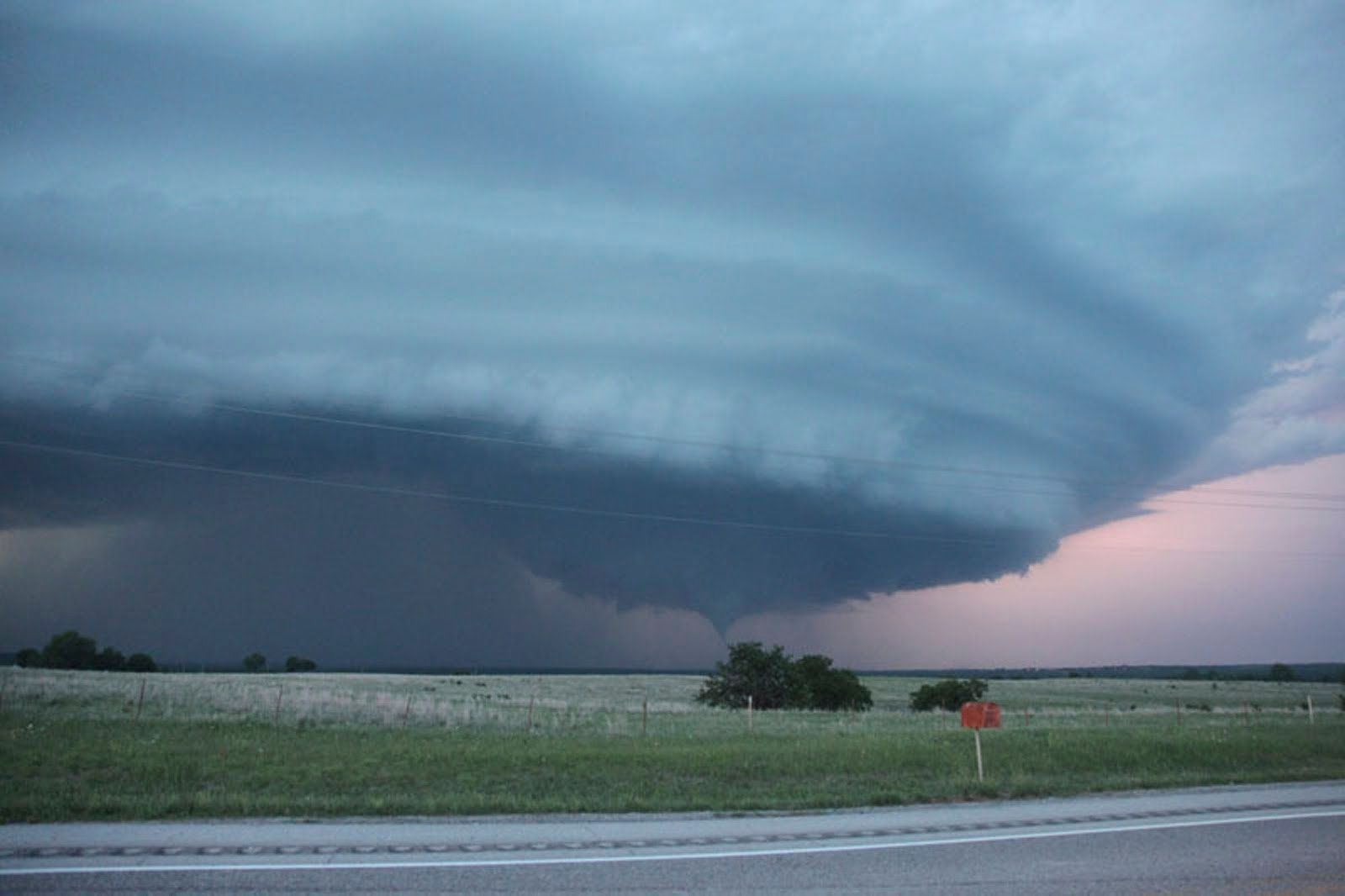 A large tornado is moving through a field near a highway.