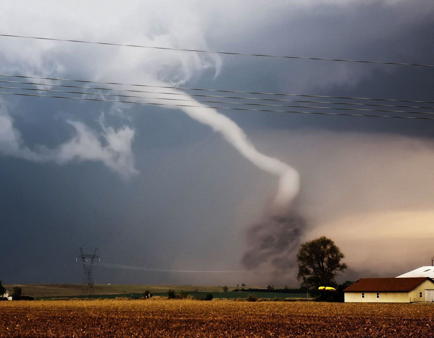 A tornado is moving through a field near a house.