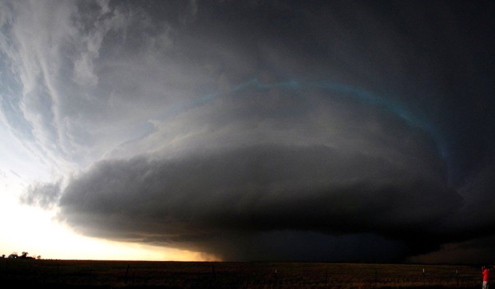 A large storm cloud is moving over a field with a rainbow in the sky.