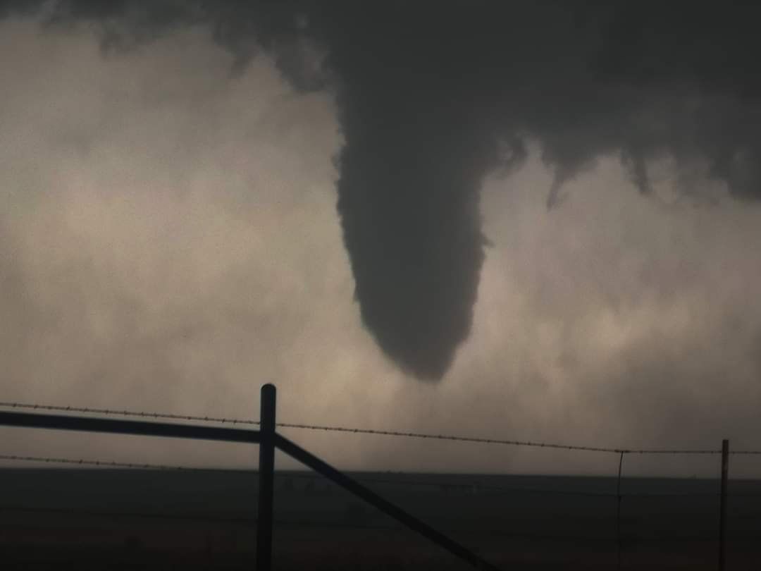A tornado is moving through a cloudy sky near a barbed wire fence.