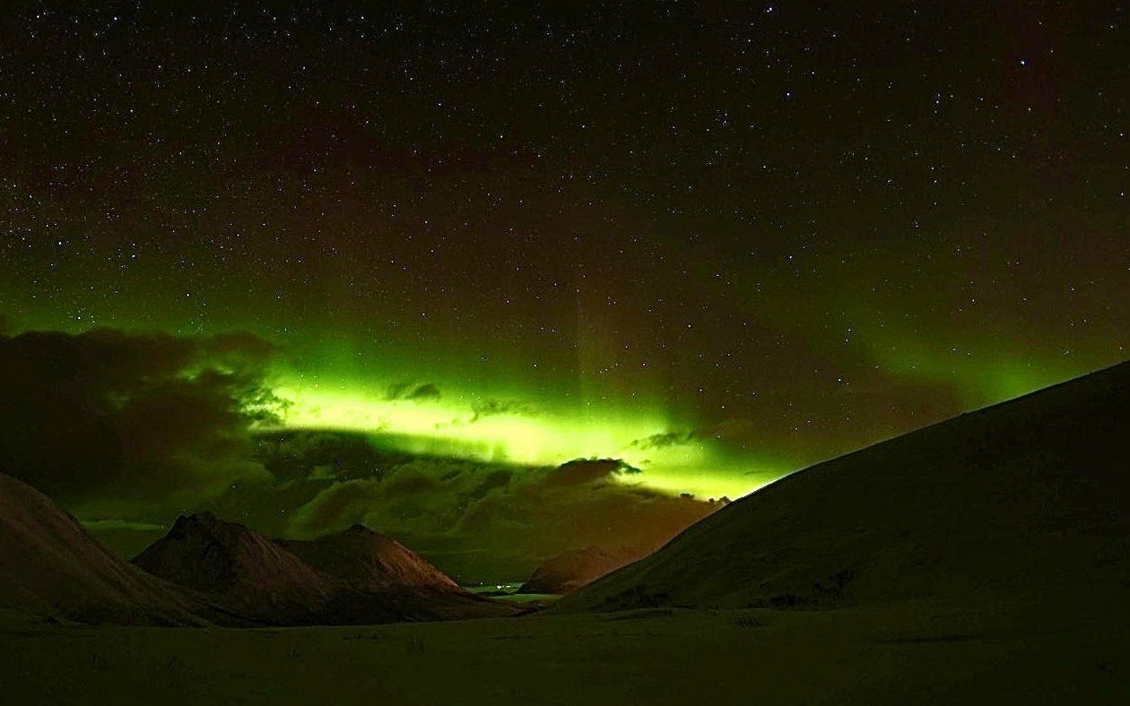 The aurora borealis is shining brightly in the night sky over a mountain range.