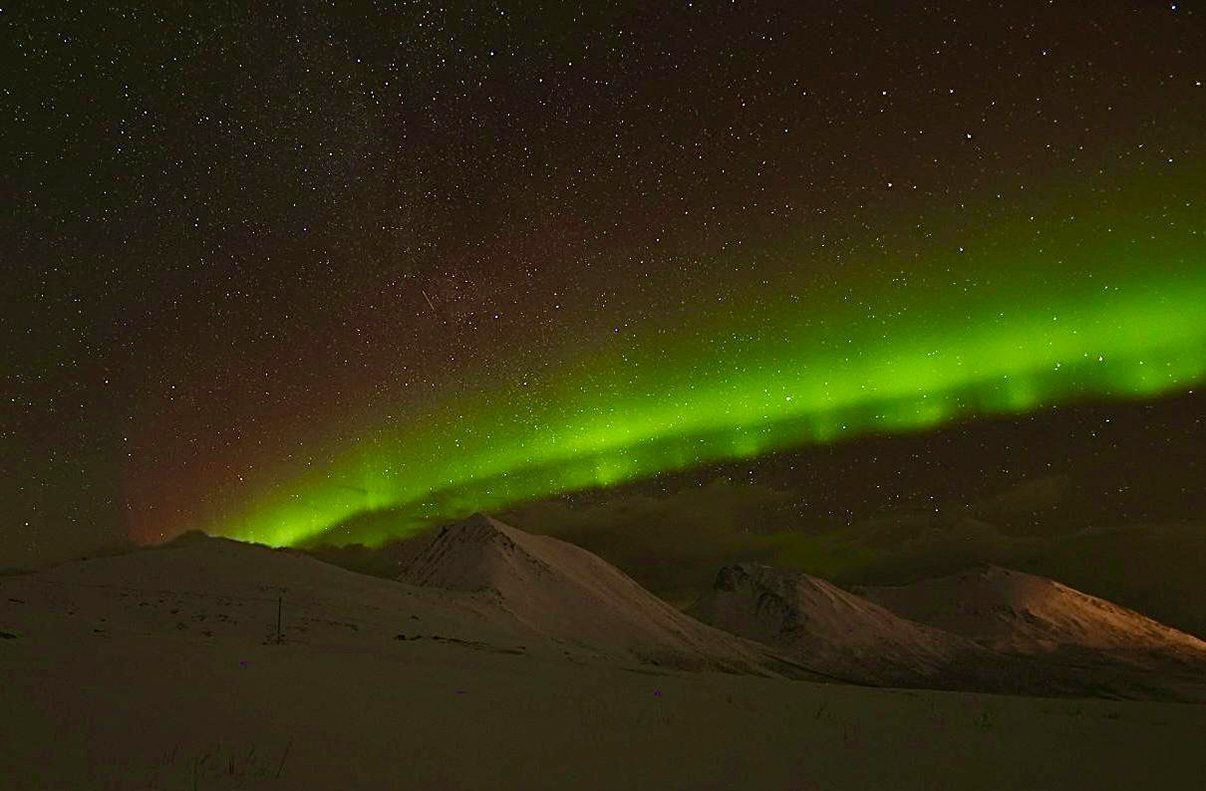 The aurora borealis is dancing in the night sky over a mountain range.