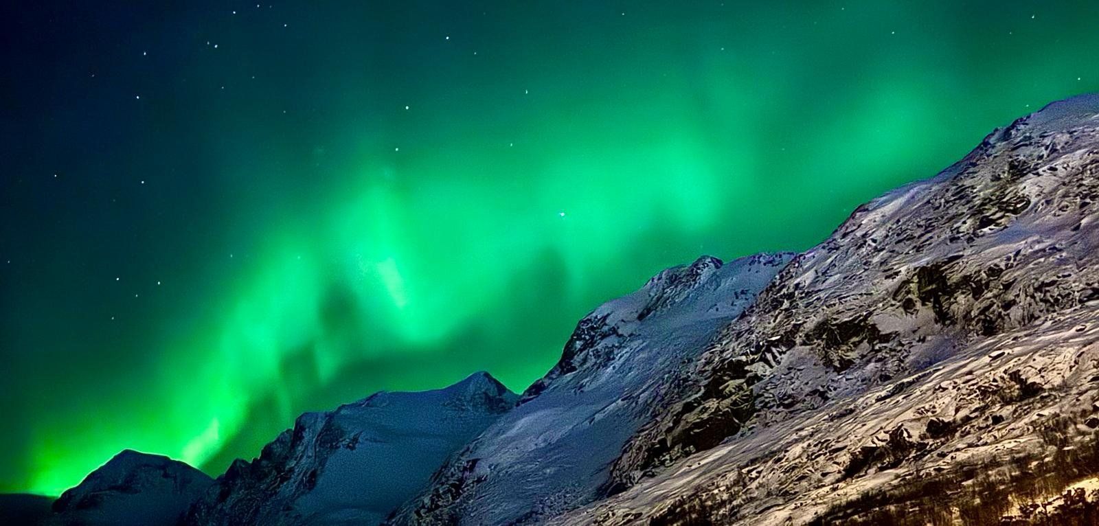 The aurora borealis is shining over a snowy mountain.