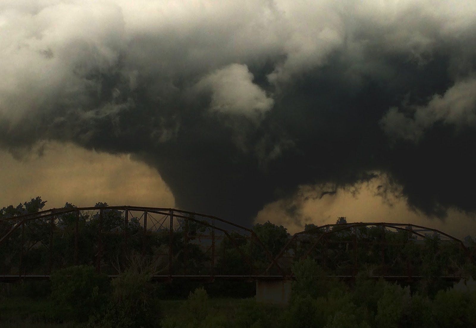 A large tornado is moving through the sky over a bridge.