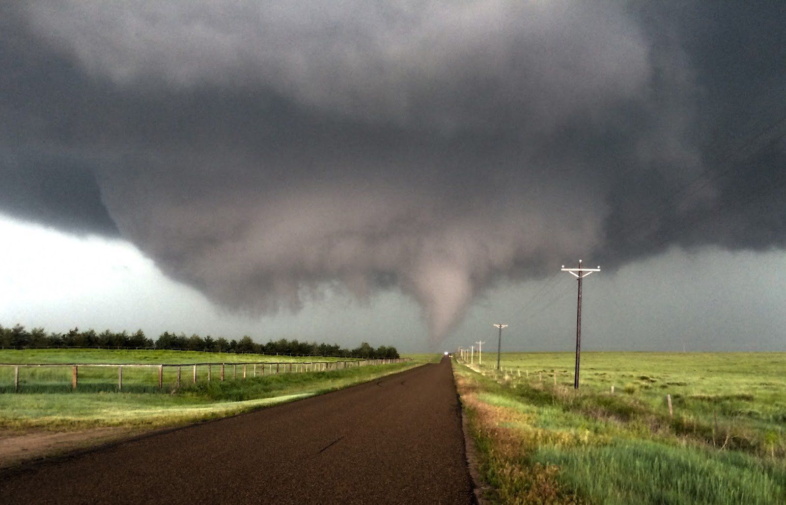 A tornado is coming down a dirt road in the middle of a field.