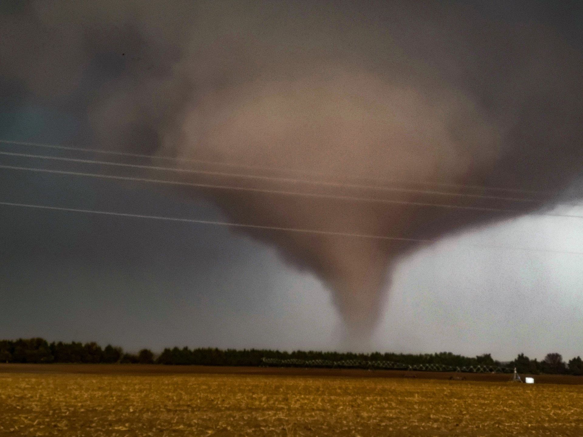 A tornado is moving through a field at night.