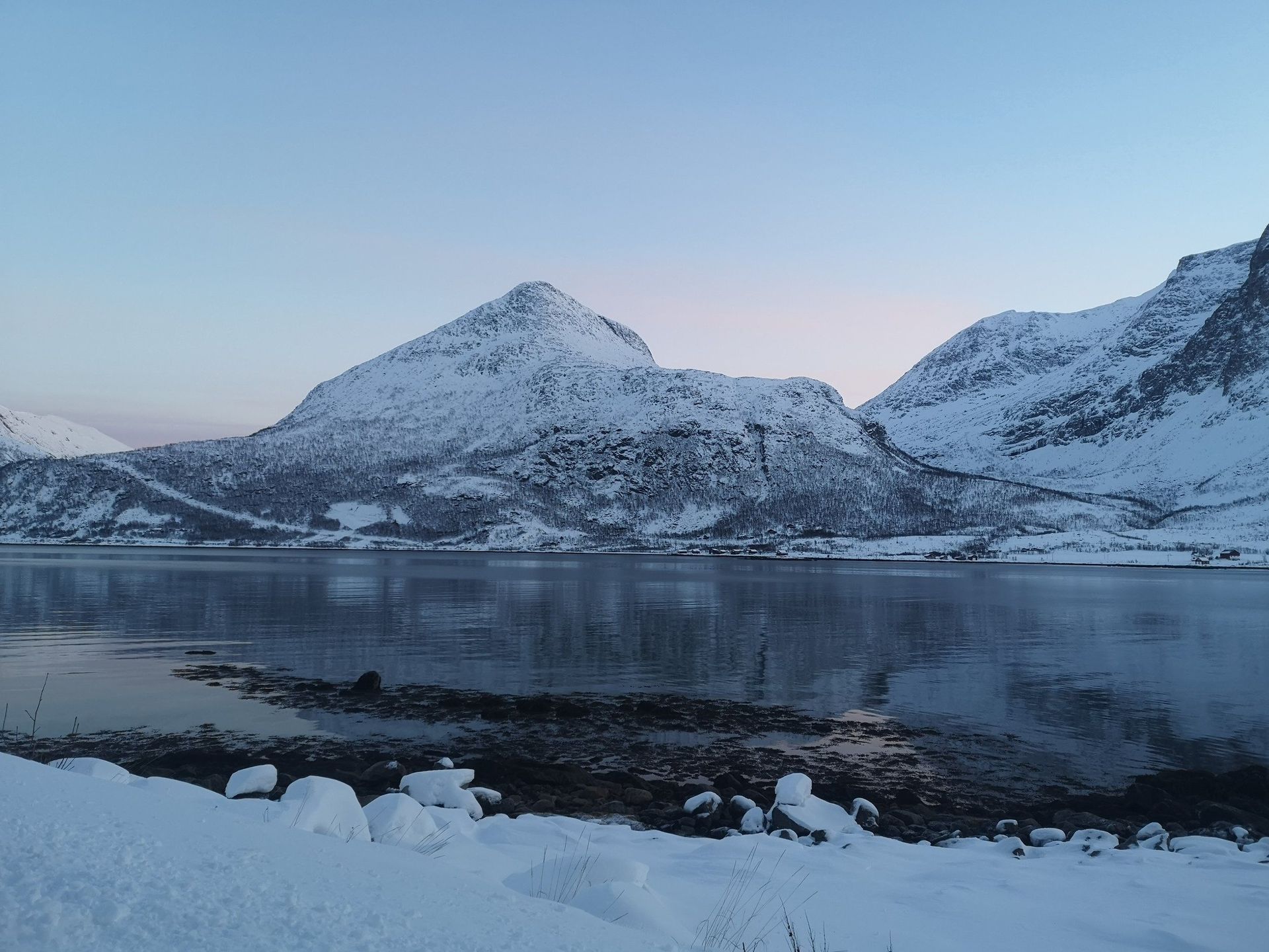 A snowy landscape with mountains and a lake in the foreground