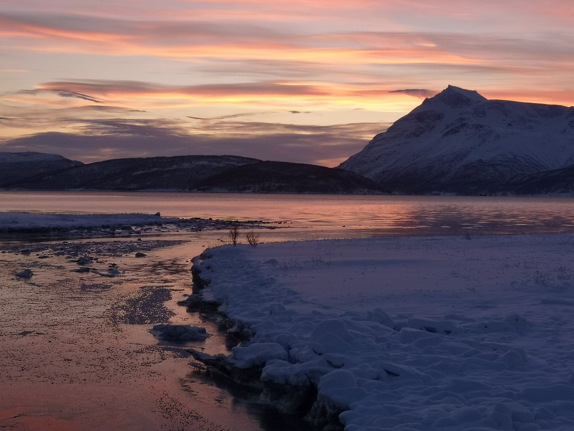 A sunset over a snowy lake with mountains in the background