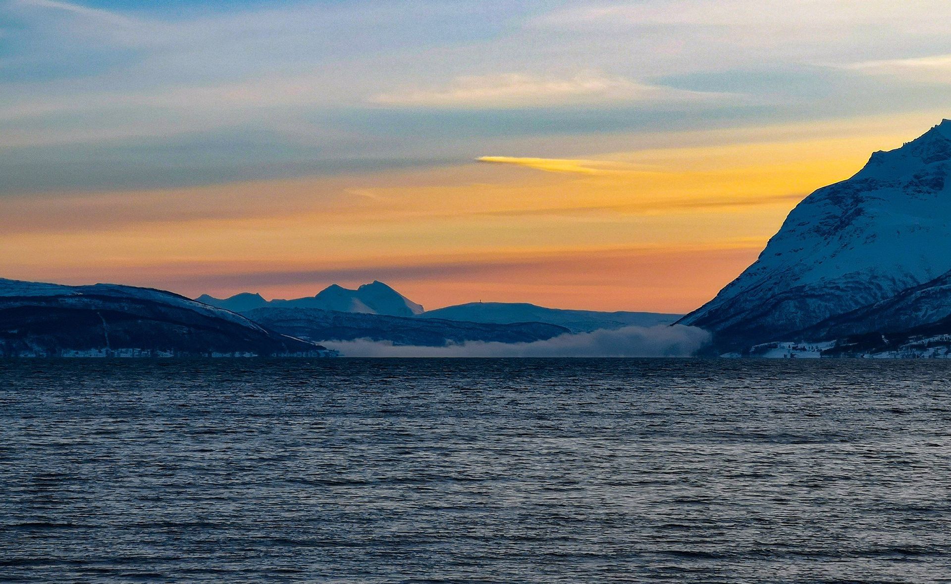 A large body of water with mountains in the background at sunset.