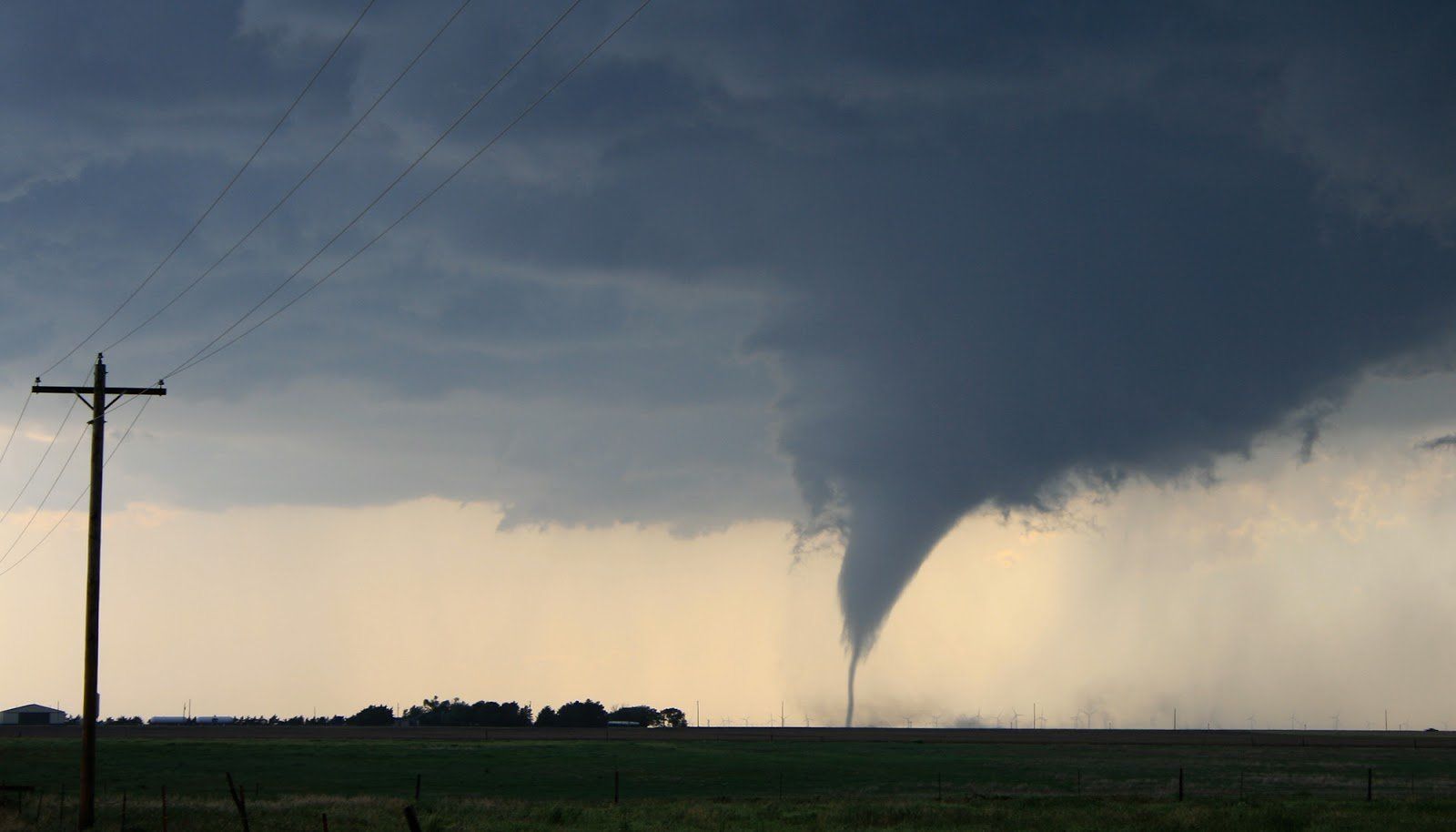 A tornado is moving through a field with a power pole in the foreground.