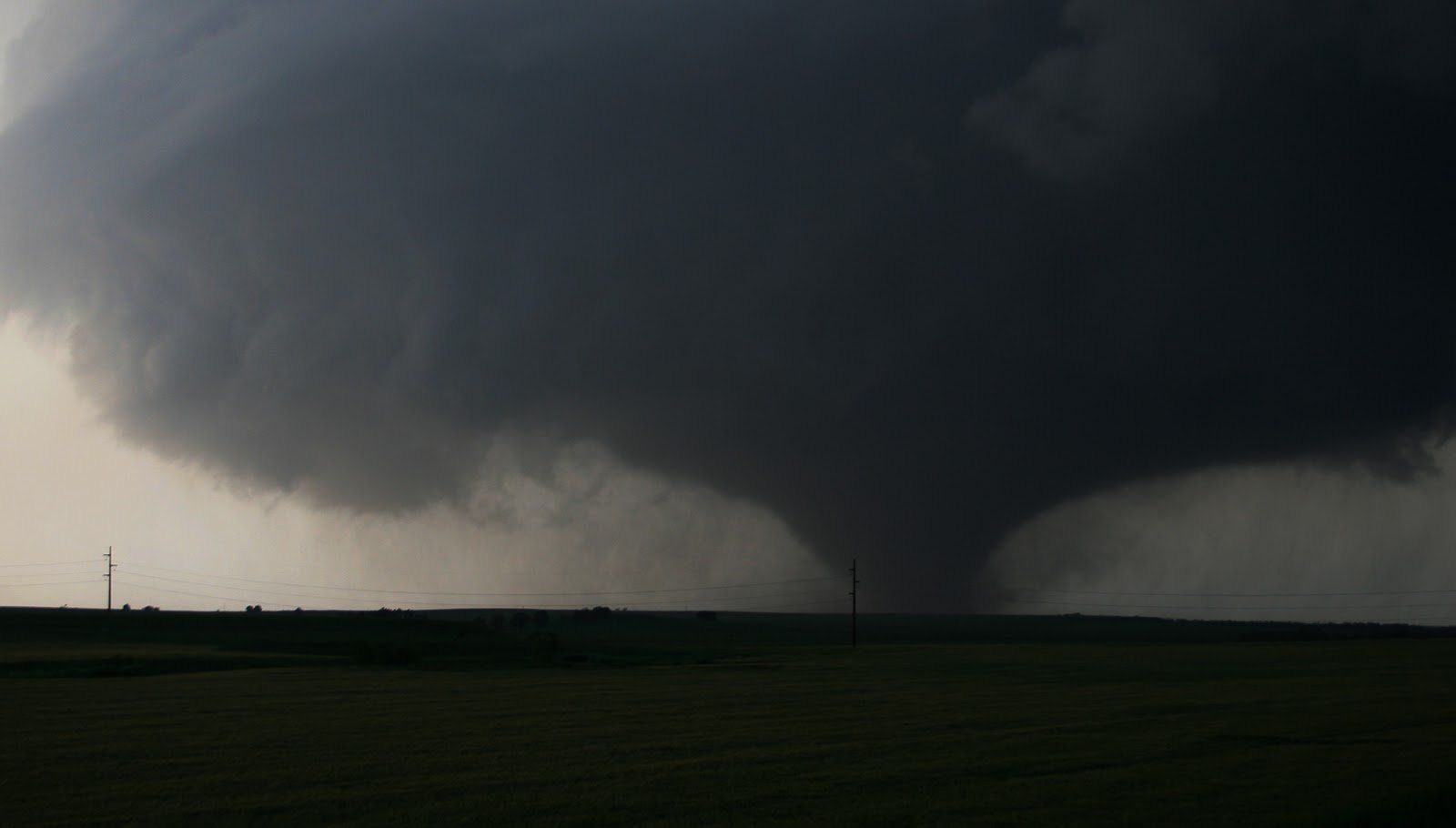 A large tornado is moving through a field at night.