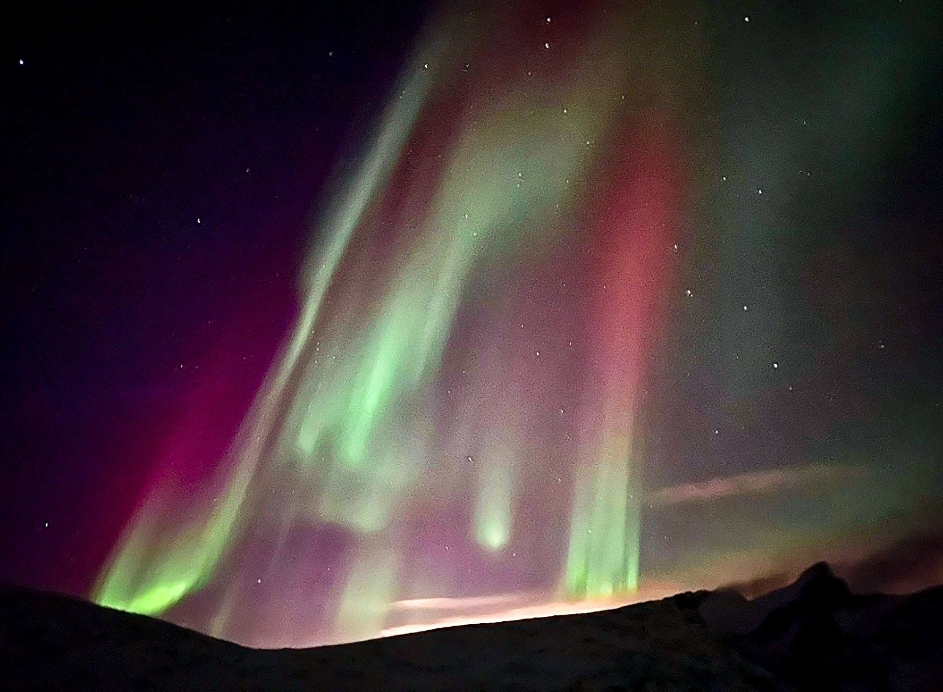 The aurora borealis is dancing in the night sky over a mountain range.