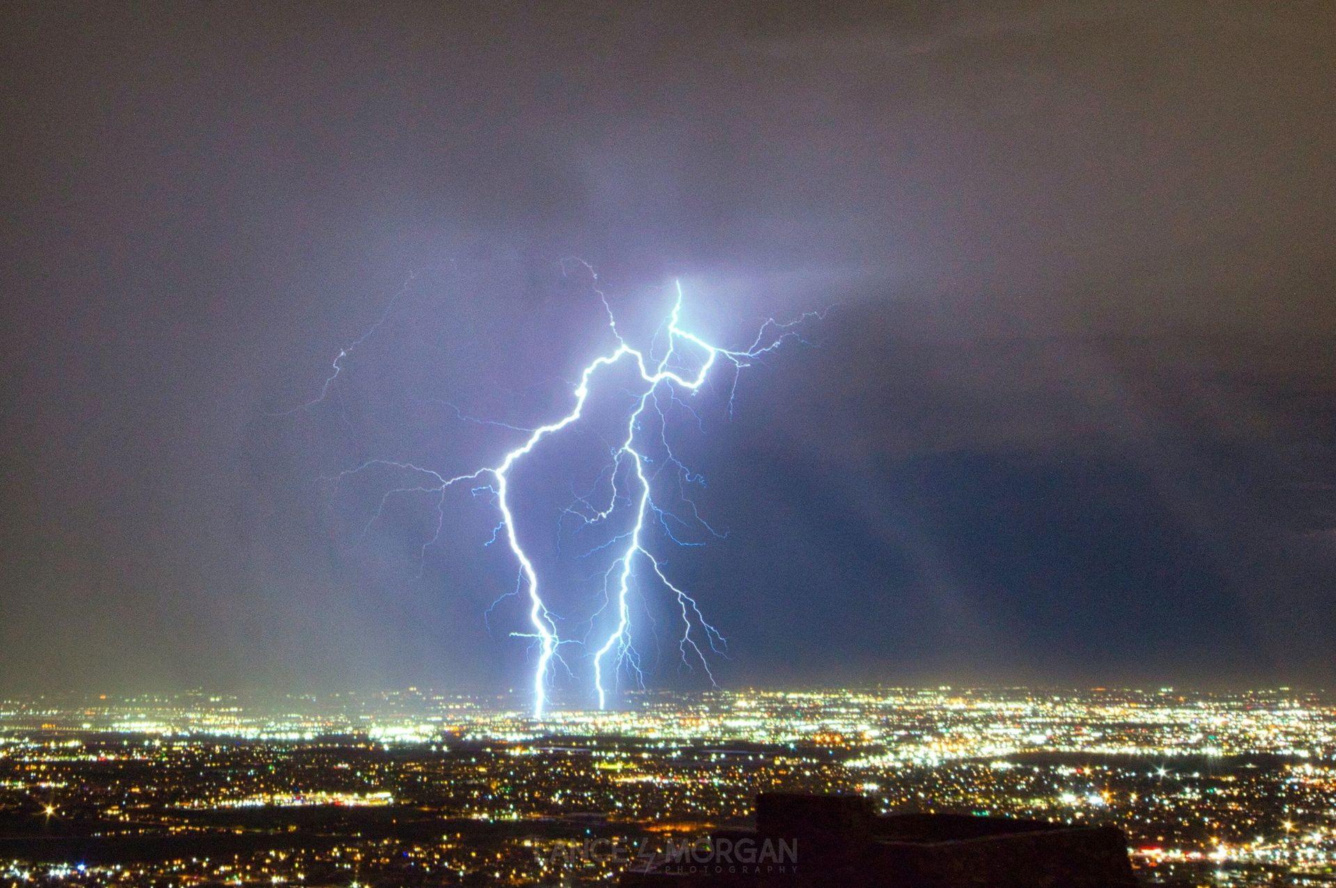 A lightning bolt strikes over a city at night.