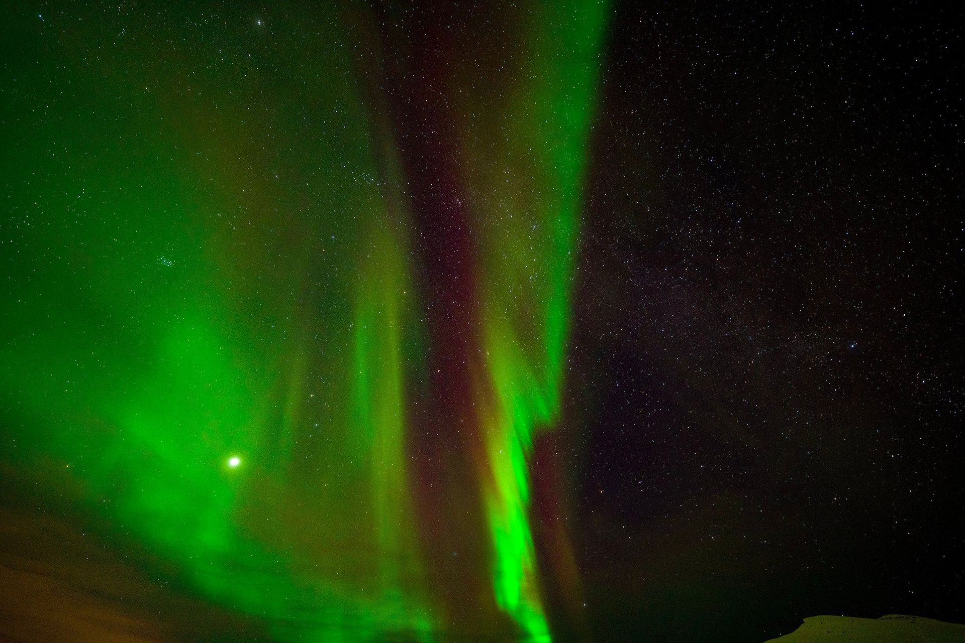 The aurora borealis is glowing green and red in the night sky.