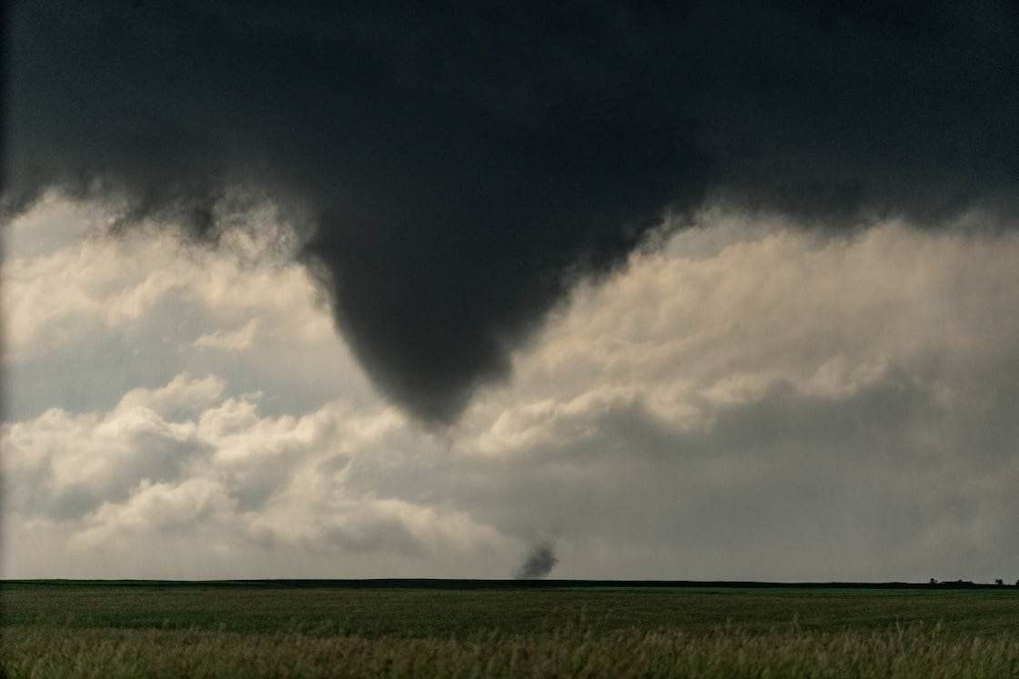 A tornado is moving through a field with a cloudy sky in the background.