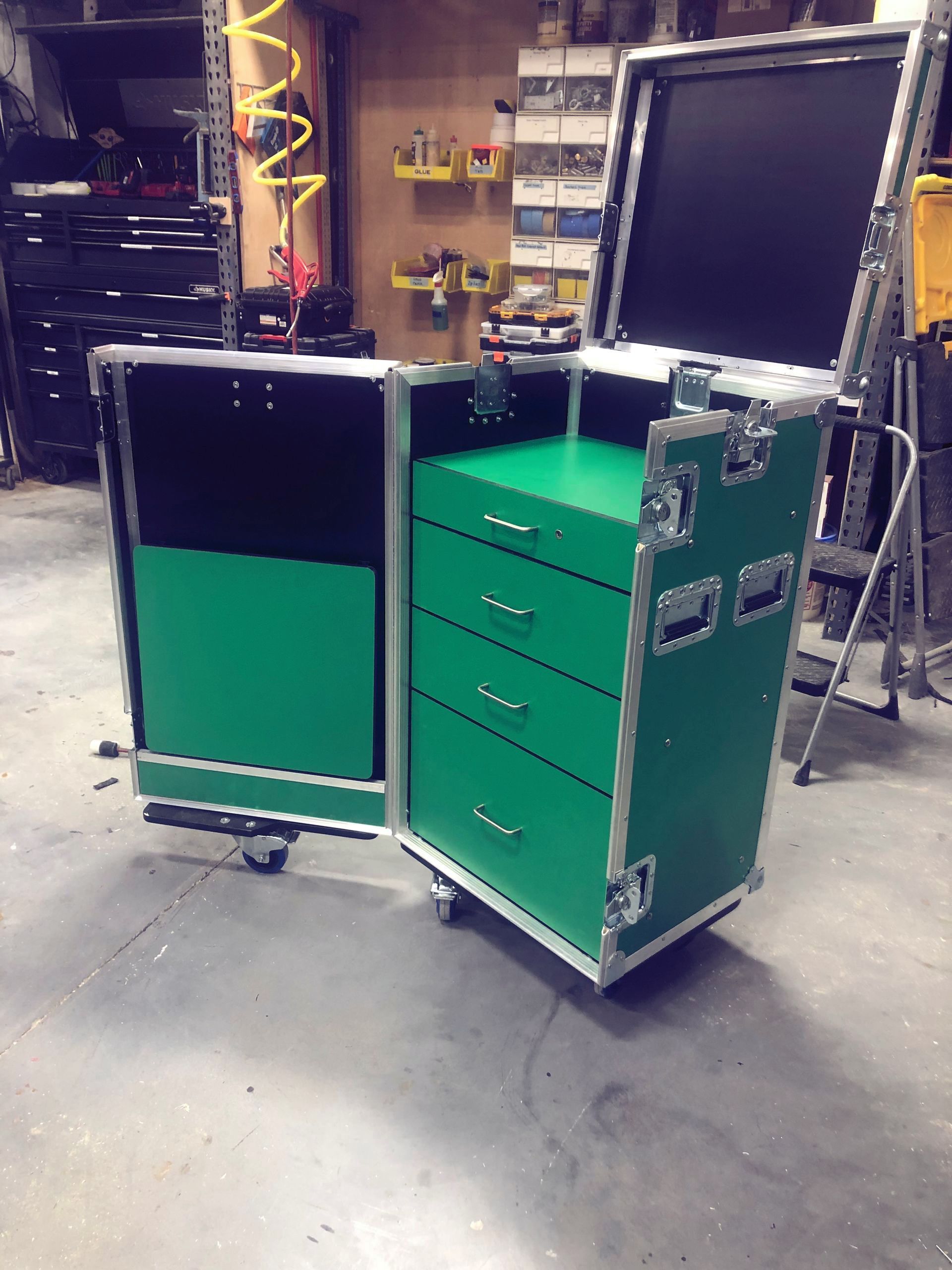Green equipment case with drawers open, displaying interior contents and wheels.