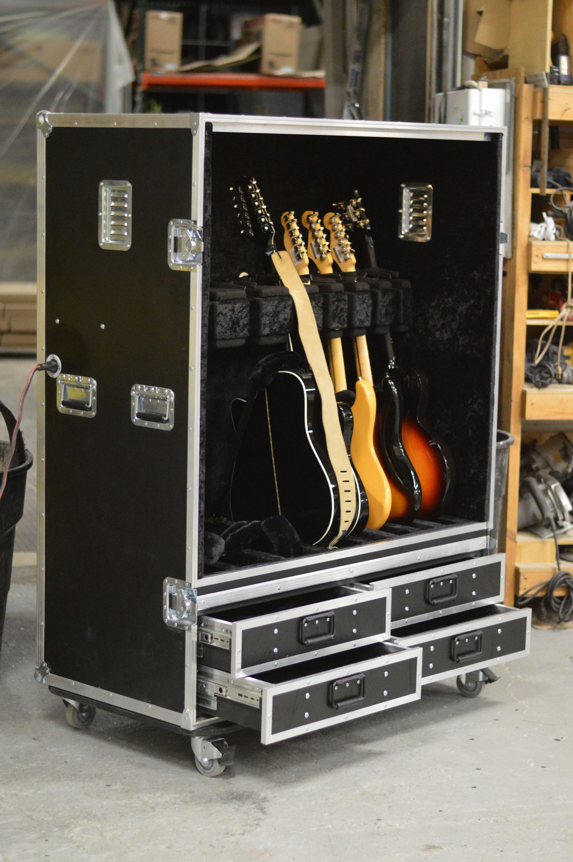 Black road case with guitars inside, three drawers open at the bottom.