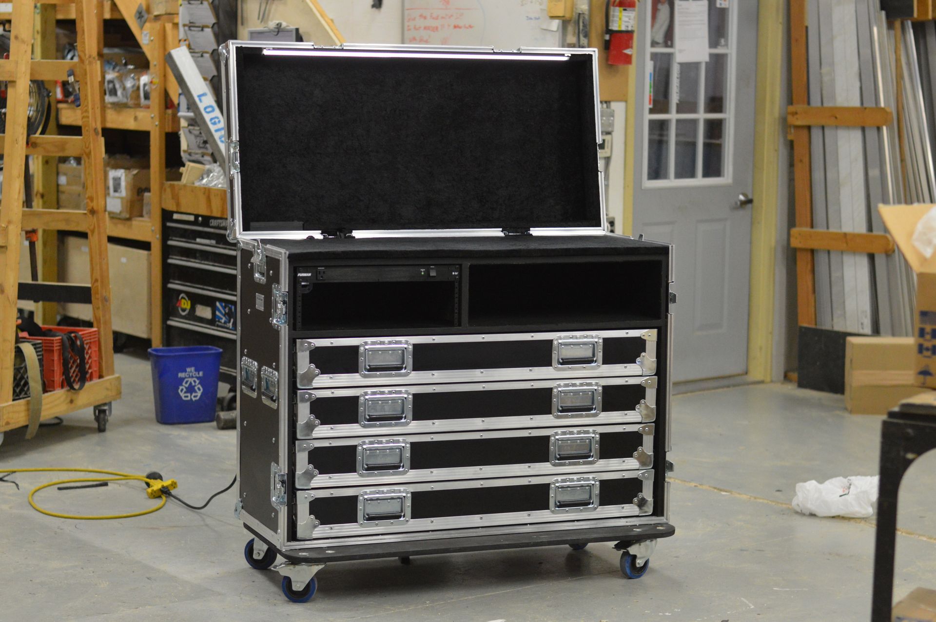 Black equipment case with open lid, drawers, and wheels; indoors in a workshop.
