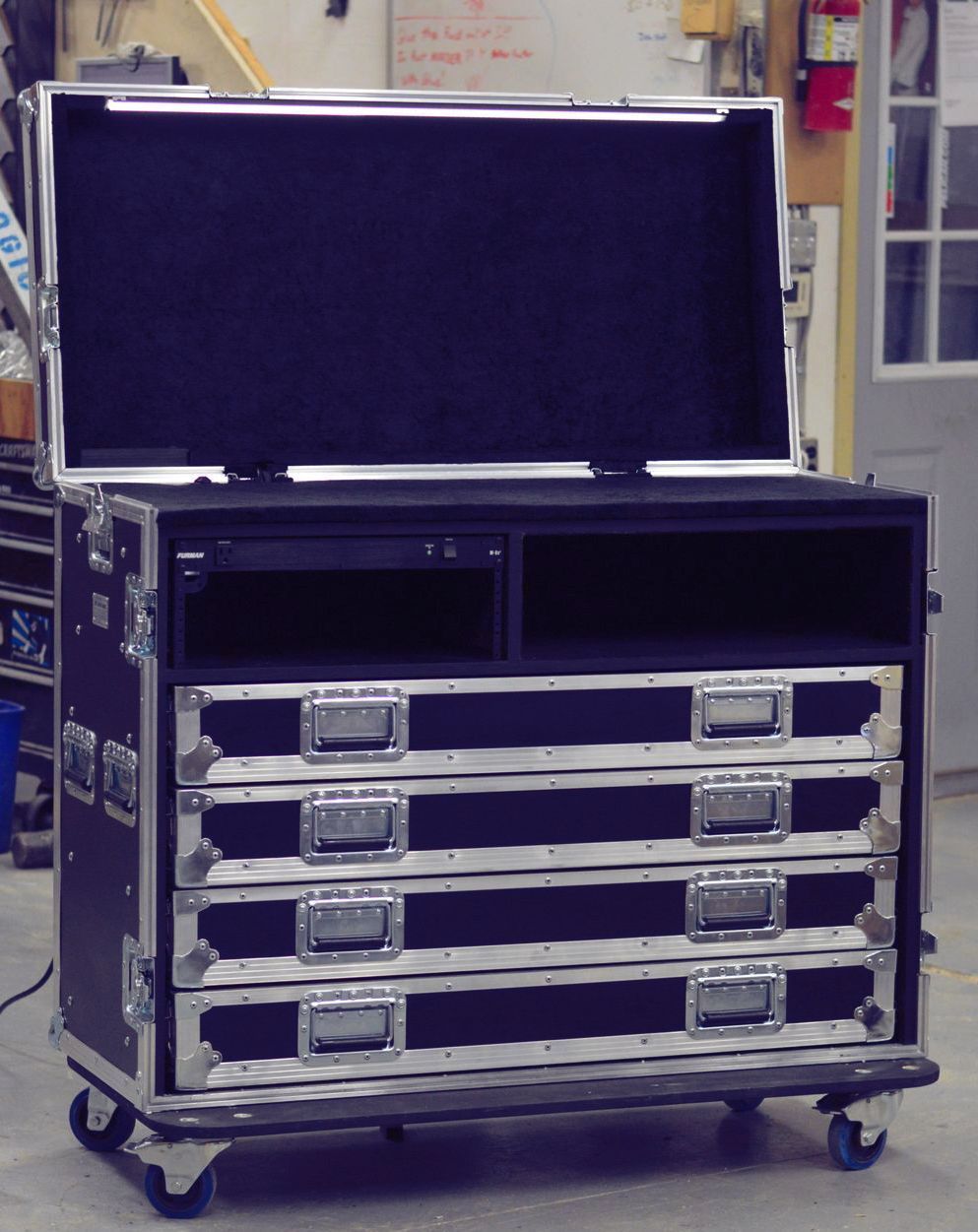Black road case with drawers and open top, on wheels, in a workshop.
