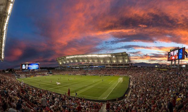 Soccer stadium at sunset; orange sky over a packed stadium, green field and players.