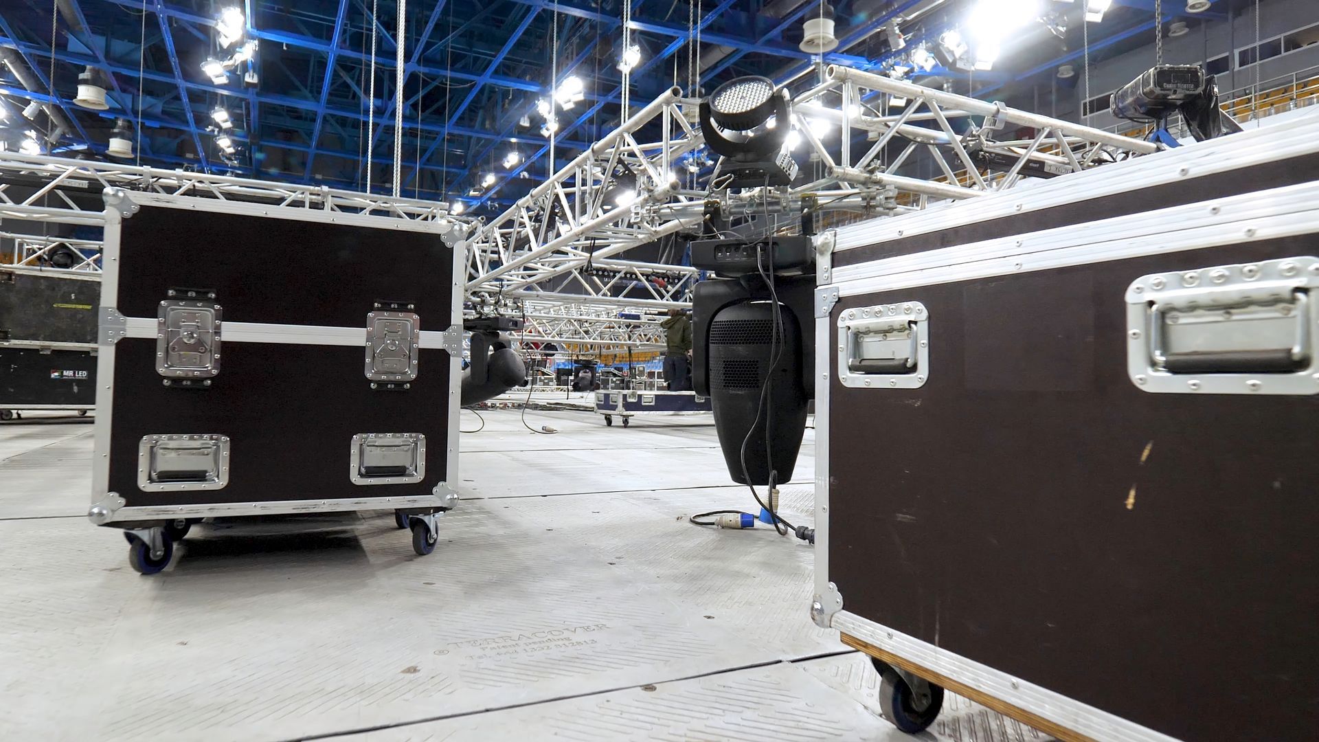 Two dark road cases on wheels in a large studio, lights and rigging in the background.