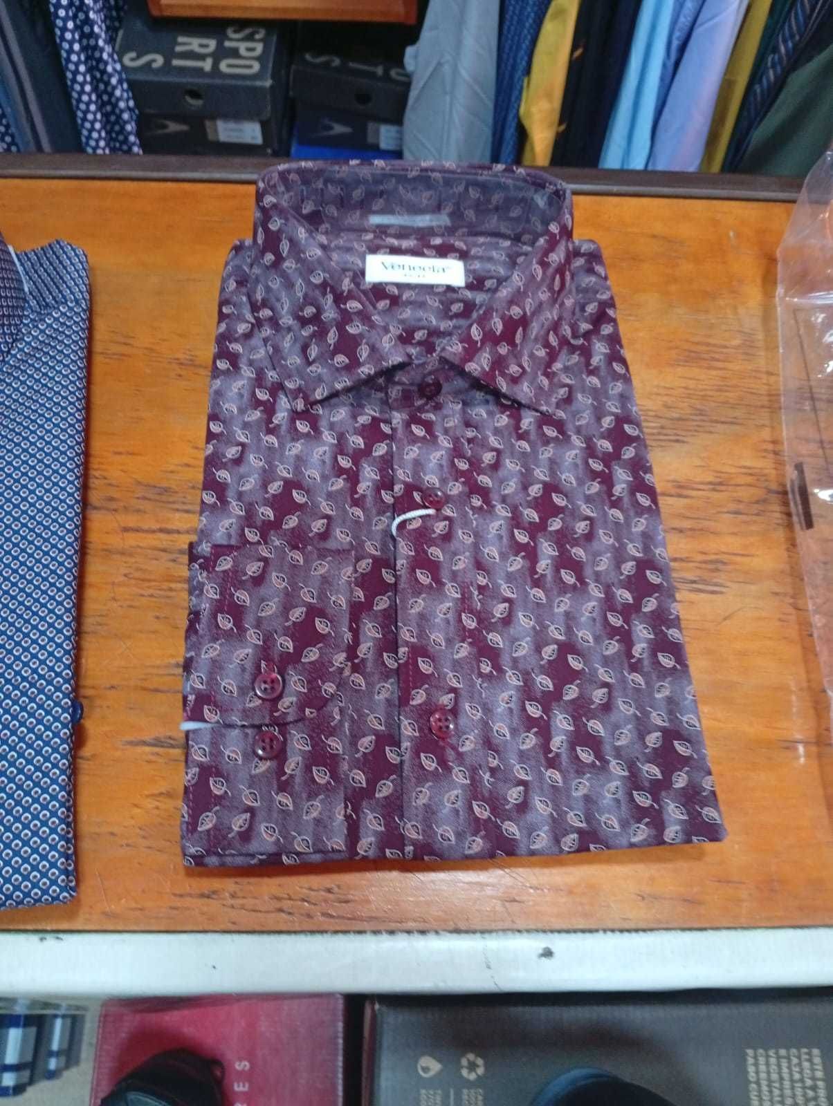 Camisa de vestir para hombre con estampado burdeos, doblada sobre una superficie de madera, expositor de tienda.