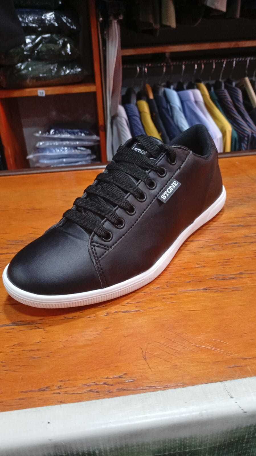 Zapatilla azul con cordones negros sobre superficie de madera, con percheros al fondo.