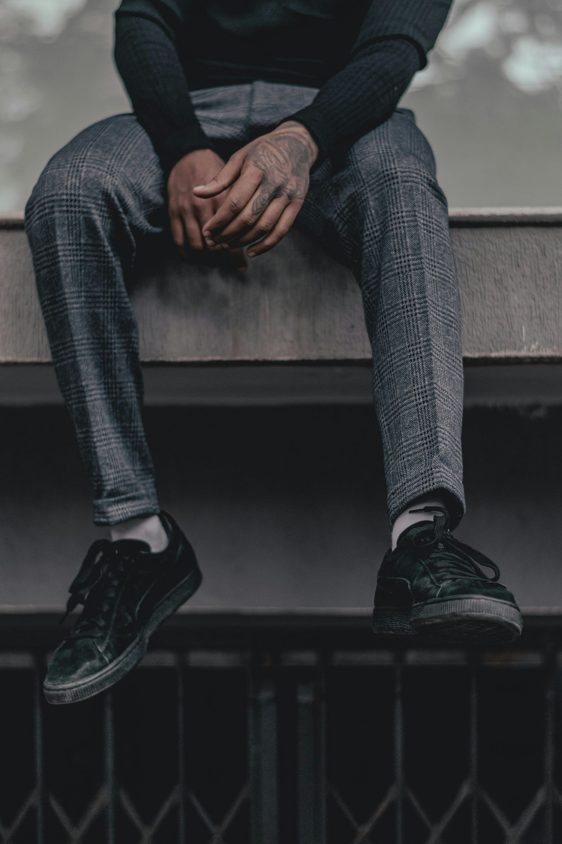 Persona sentada, con las manos entrelazadas, sobre una cornisa, vistiendo pantalones grises estampados
