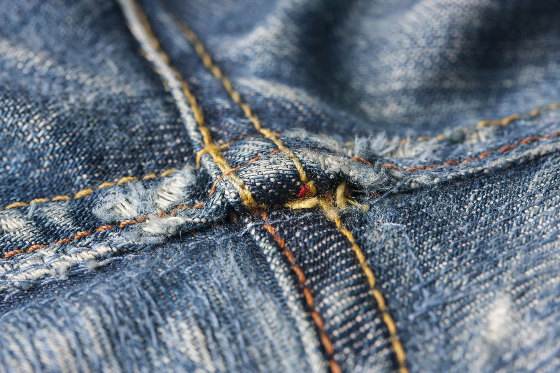 Primer plano de costura de jeans de mezclilla azul con hilo color canela y naranja.