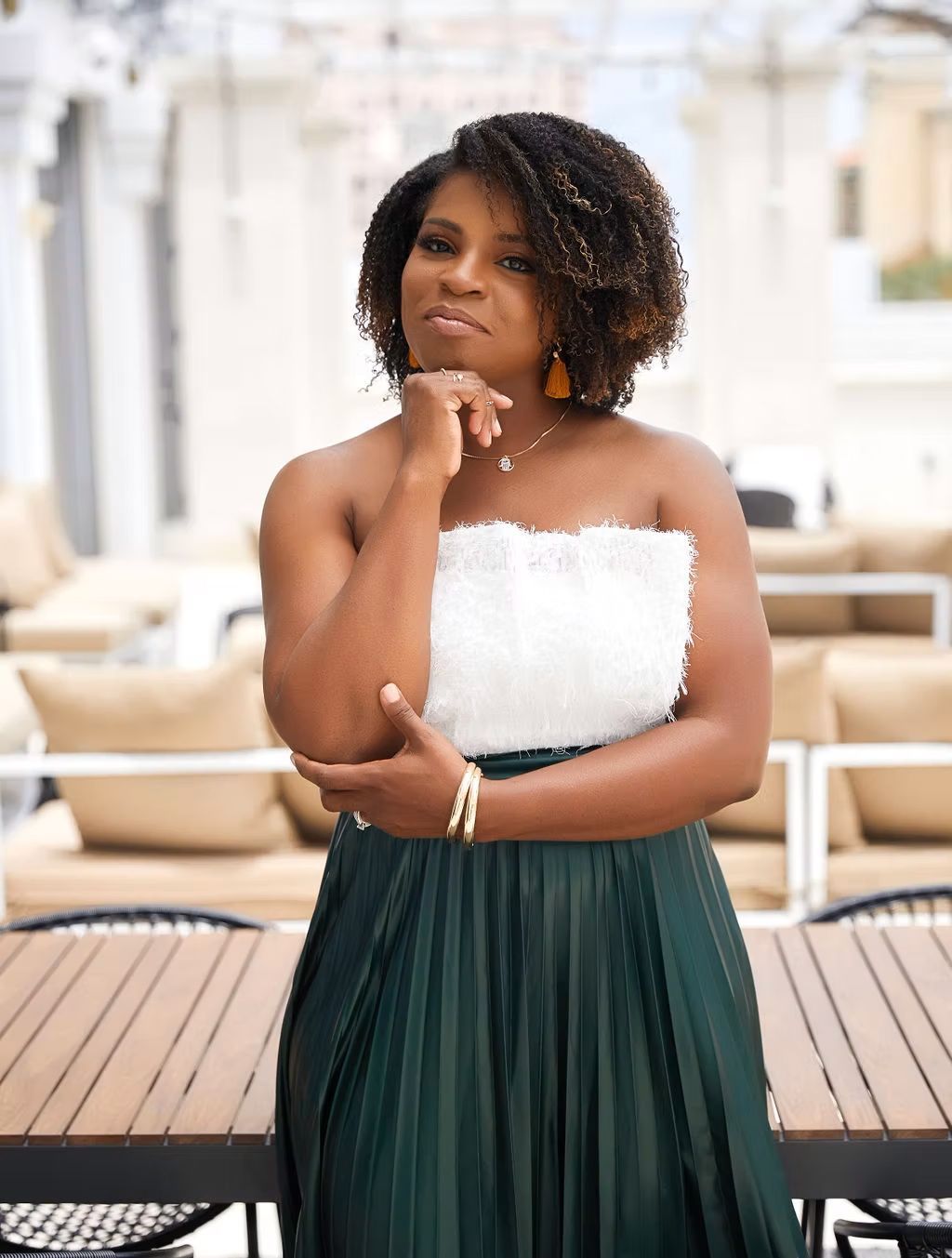 A woman in a white top and green skirt is standing in front of a wooden table.
