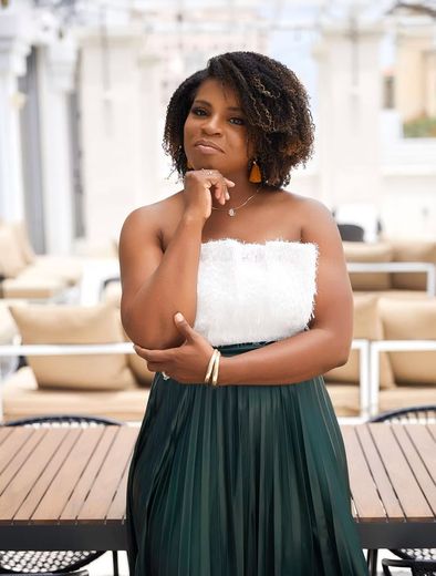A woman in a white top and green skirt is standing in front of a wooden table.