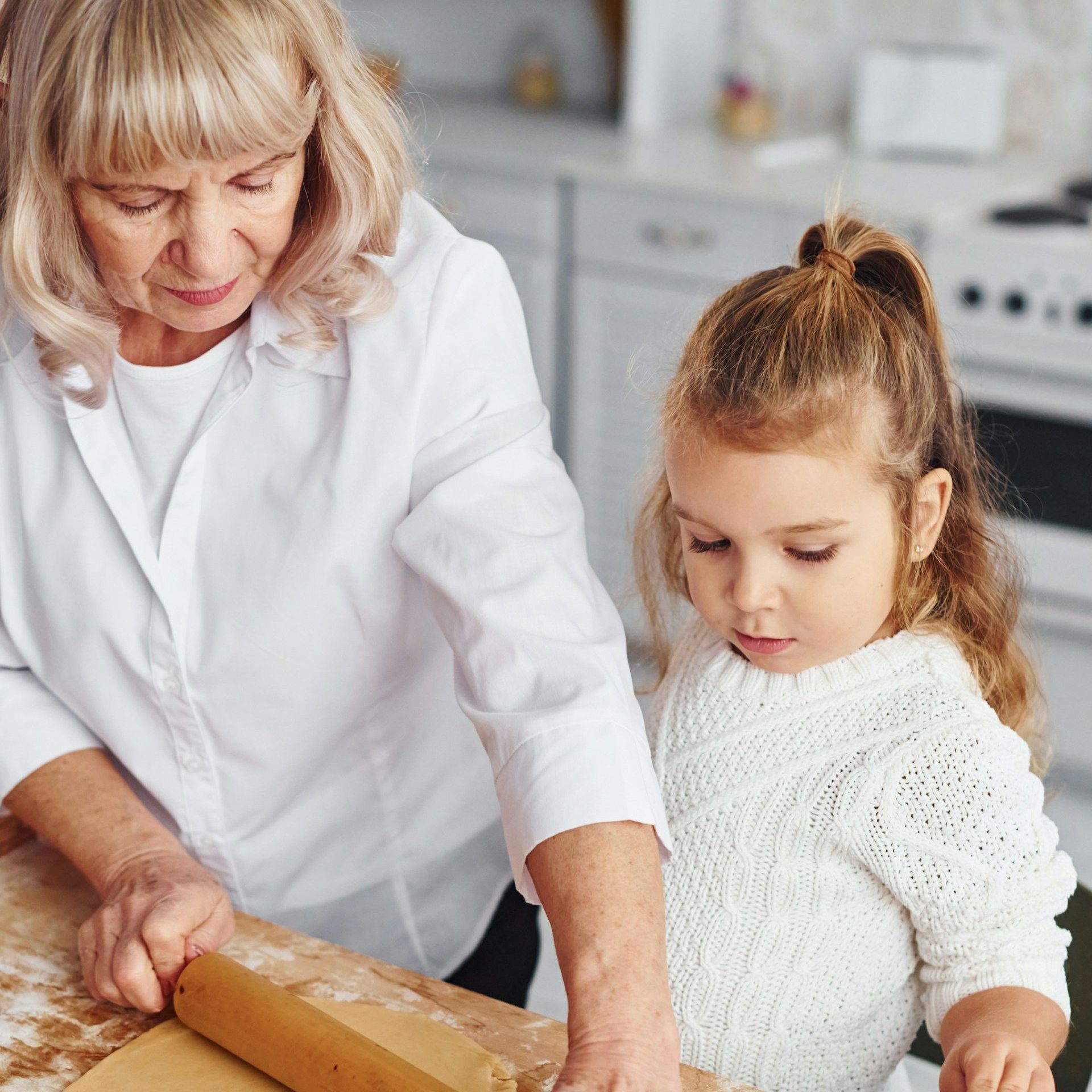 A woman and a little girl are rolling dough on a table.