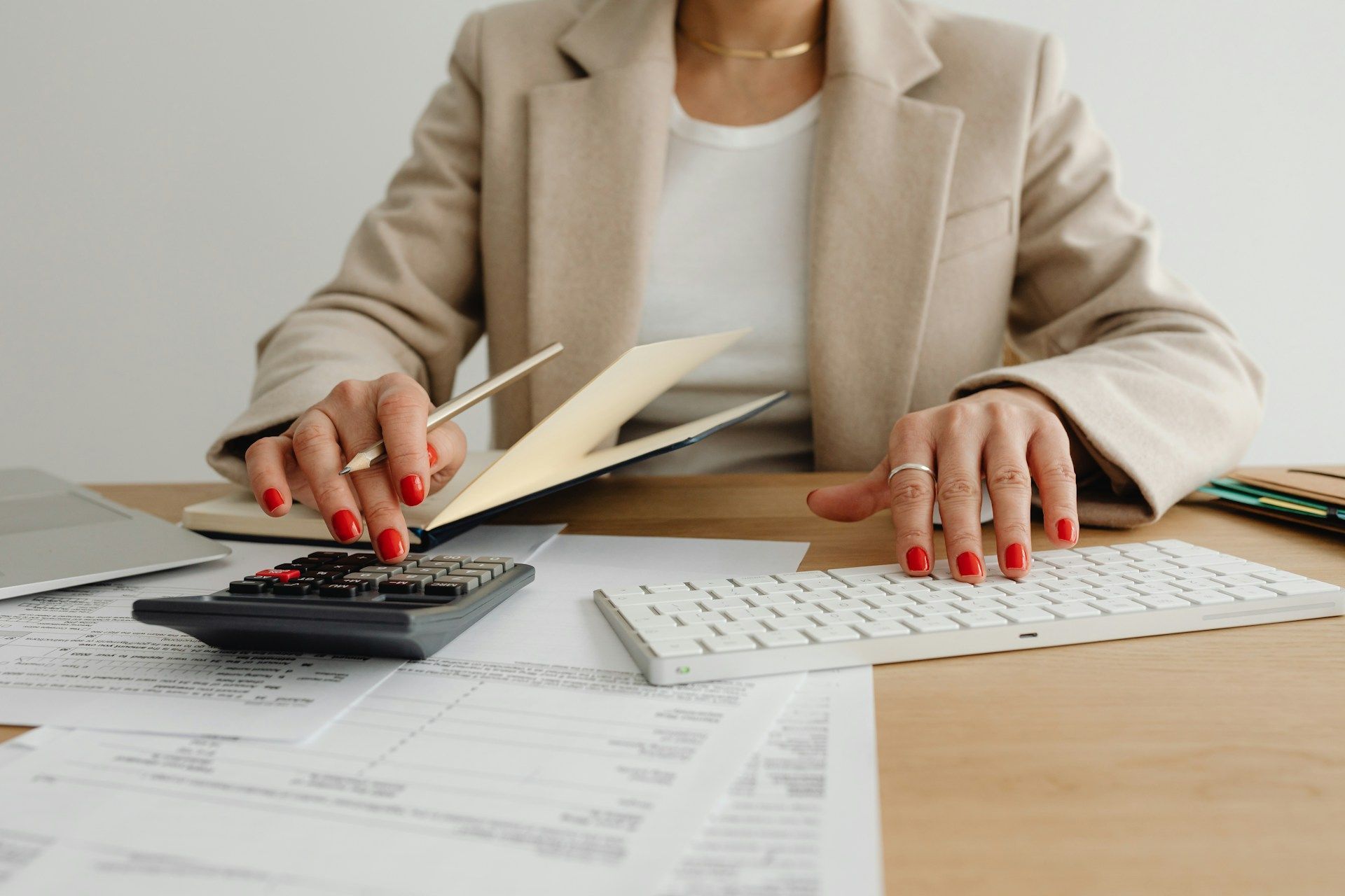 A woman is sitting at a desk using a calculator and a keyboard.