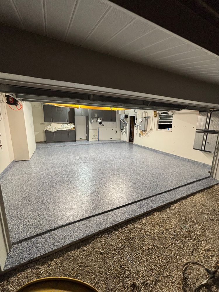 A garage with a concrete floor and a garage door open.