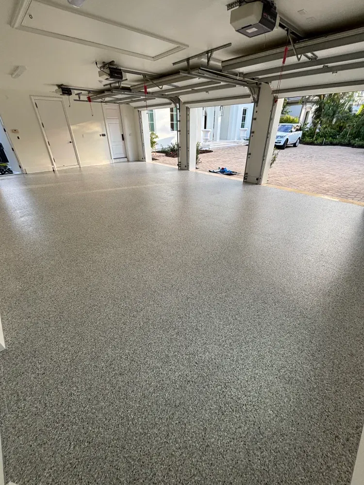 A garage with a concrete floor and a garage door open.