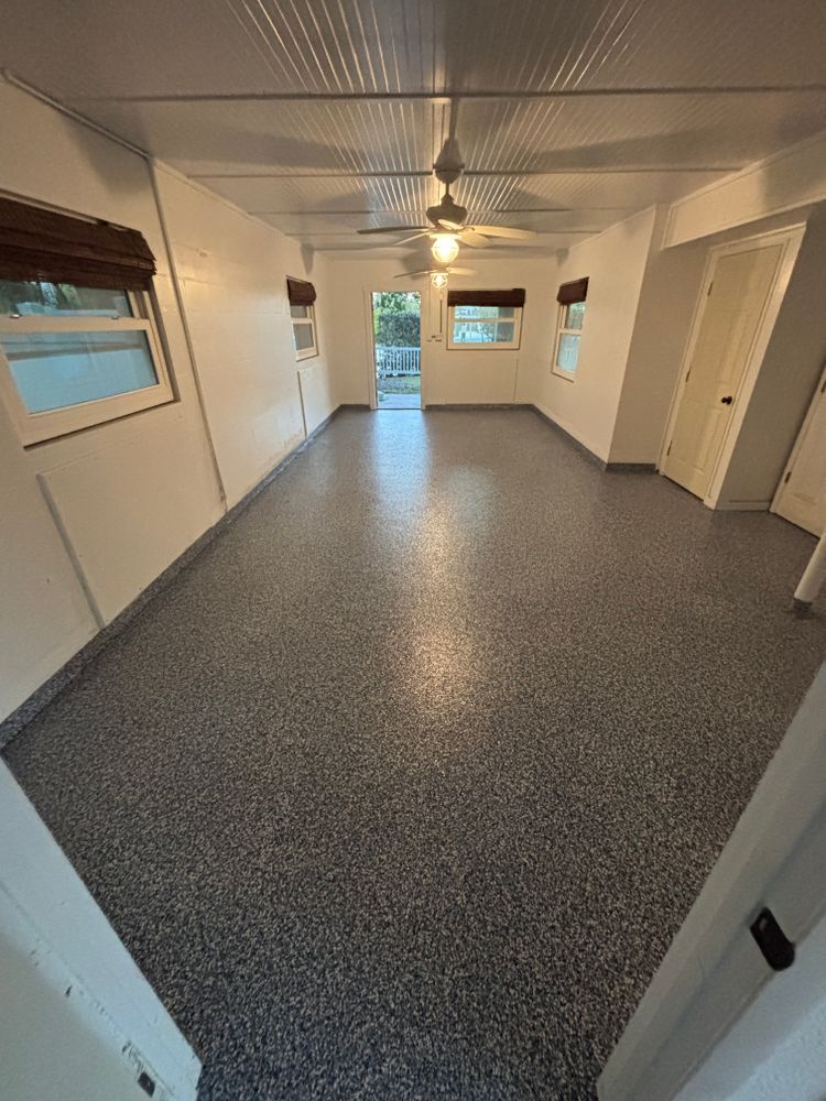 A large empty room with a ceiling fan and a gray floor.