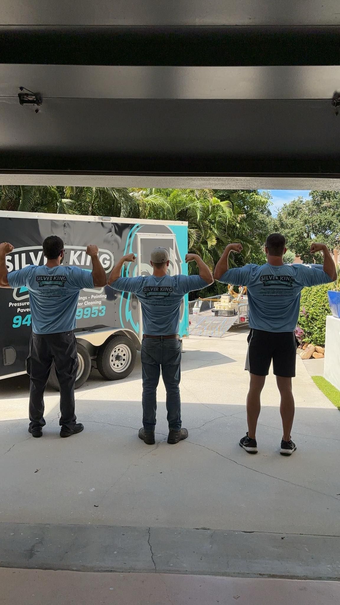 Three men are standing in front of a truck with their arms outstretched.