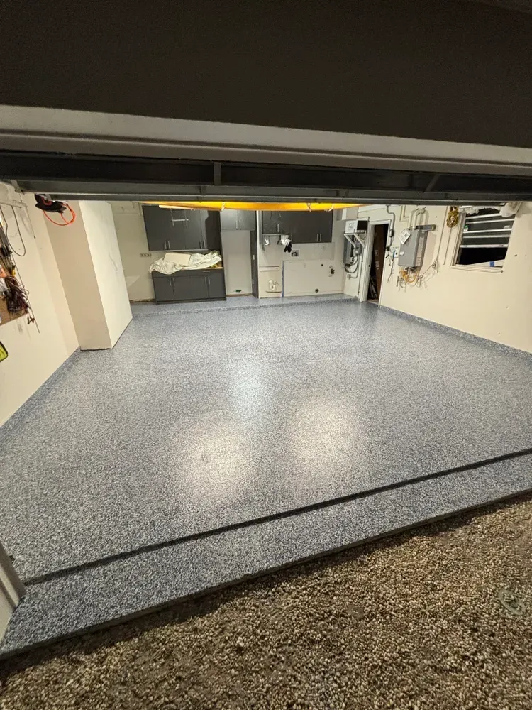 A garage with a concrete floor and a garage door open.