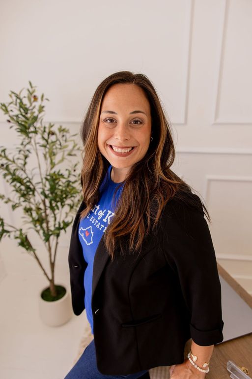 A woman is sitting at a desk with a laptop and a vase of flowers.