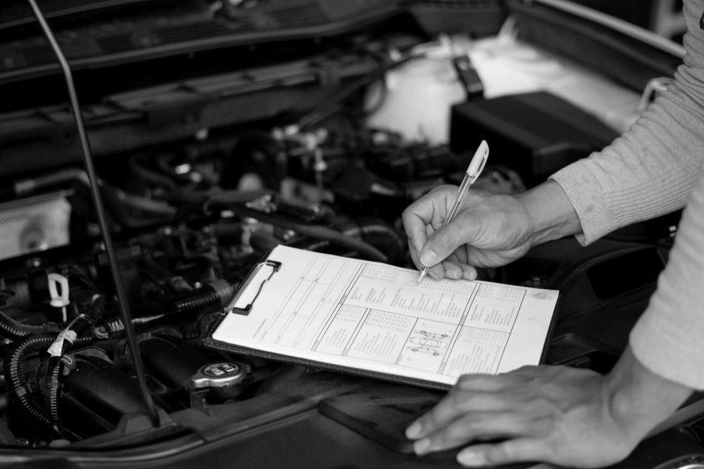 A Man Is Writing On A Clipboard In Front Of A Car Engine — Advanced Auto Tech In Port Macquarie, NSW
