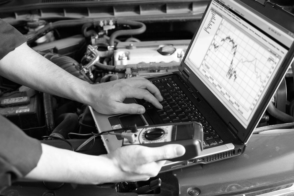 A Man Is Working On A Laptop Computer Under The Hood Of A Car — Advanced Auto Tech In Port Macquarie, NSW