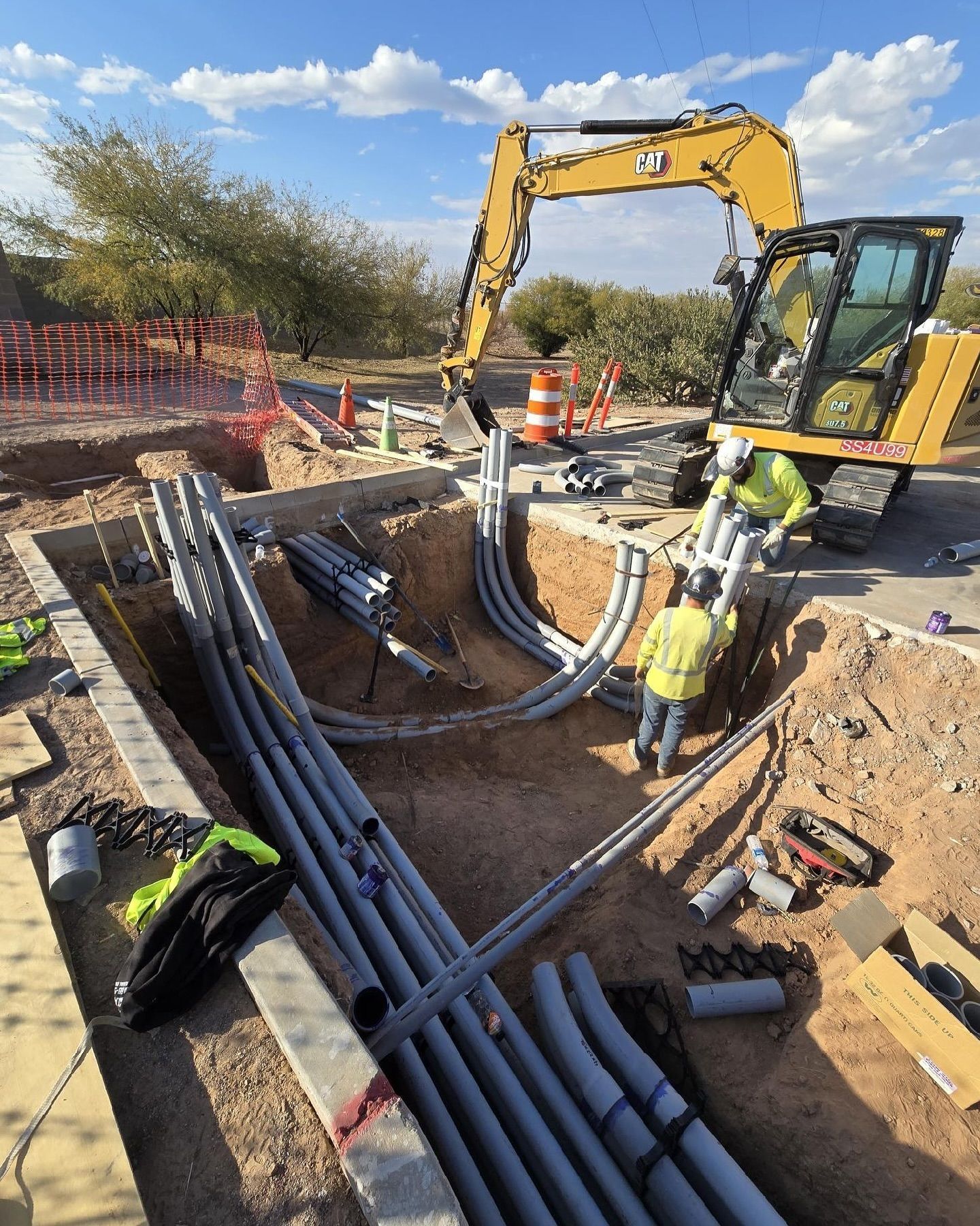 Construction crew installing underground pipes beside an excavator at a trench site