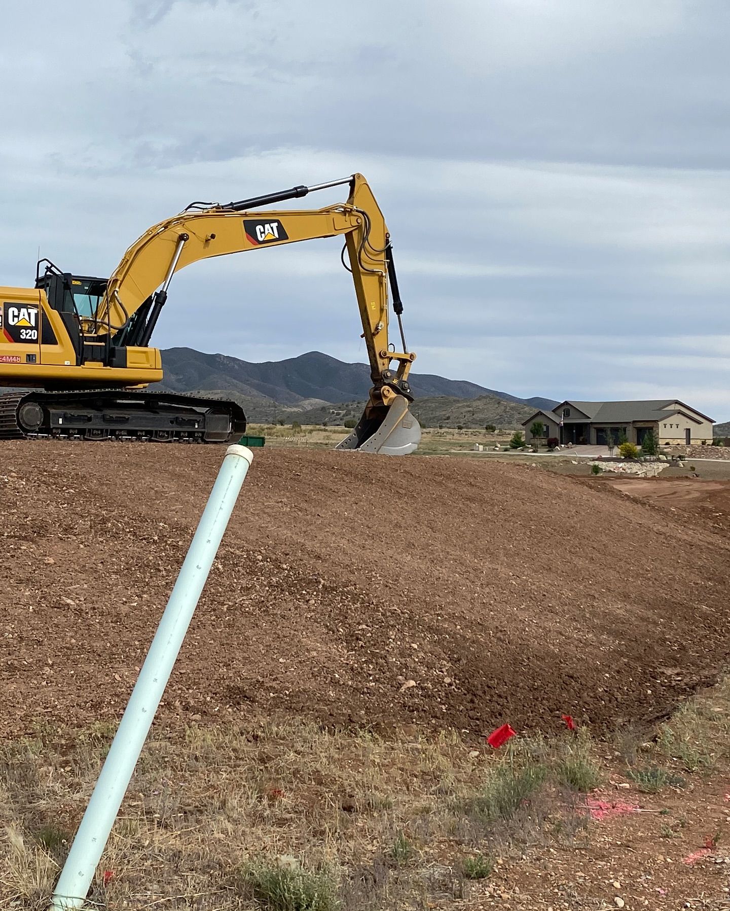 Yellow excavator on a dirt mound at a construction site under a cloudy sky.