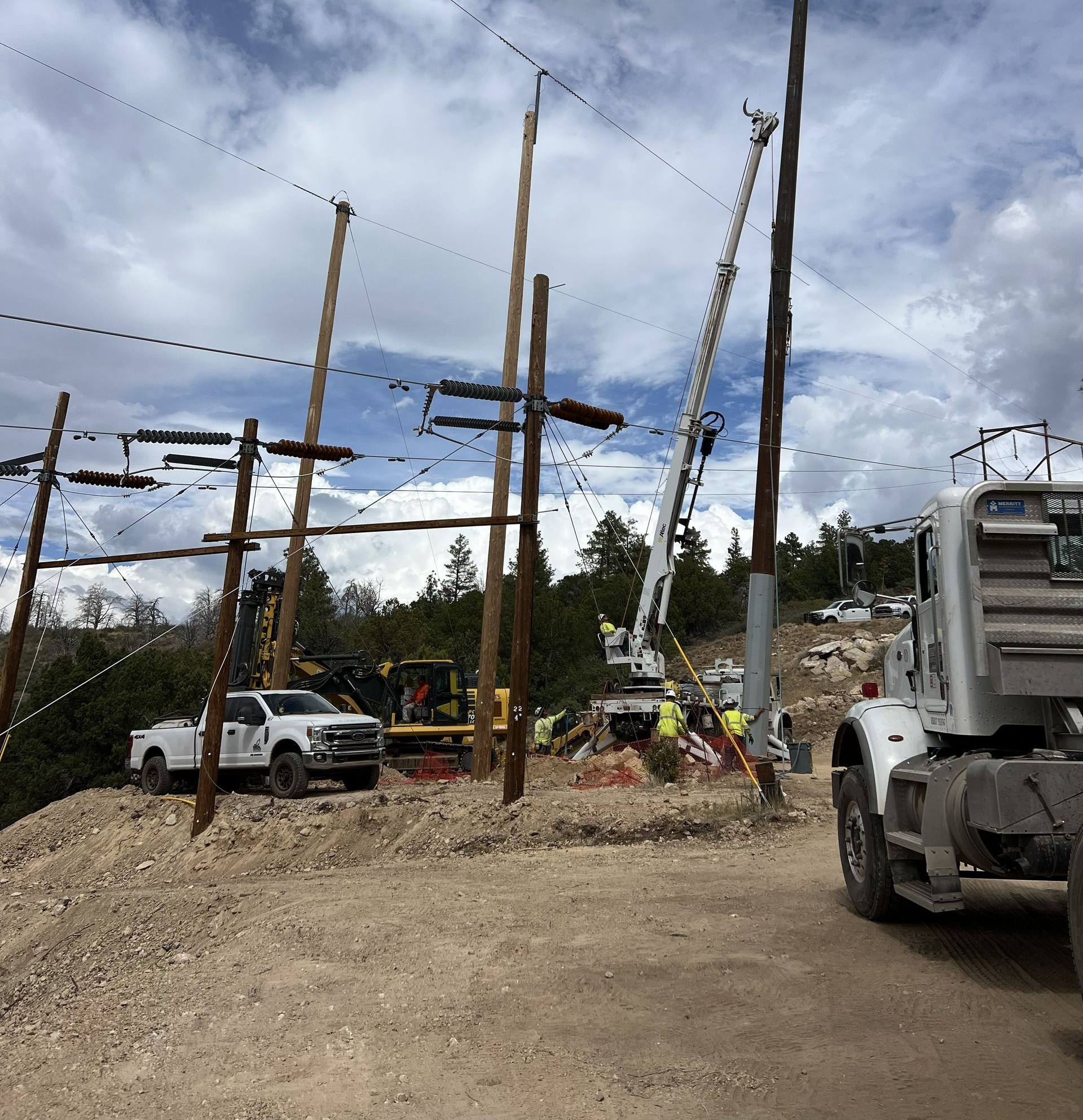 Utility workers repairing power lines with trucks and tall poles at a rural roadside site.