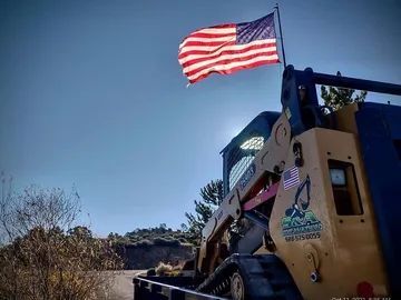American flag waving above a yellow construction vehicle in a sunny outdoor setting