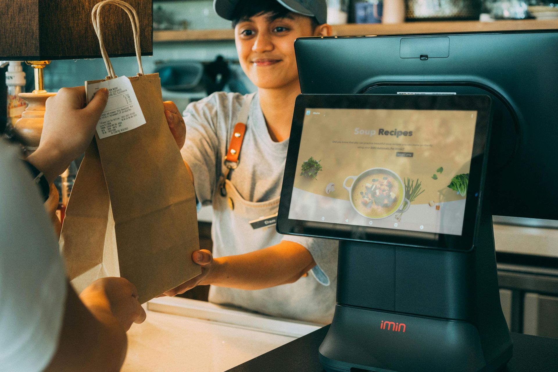A woman is holding a paper bag in front of a computer.