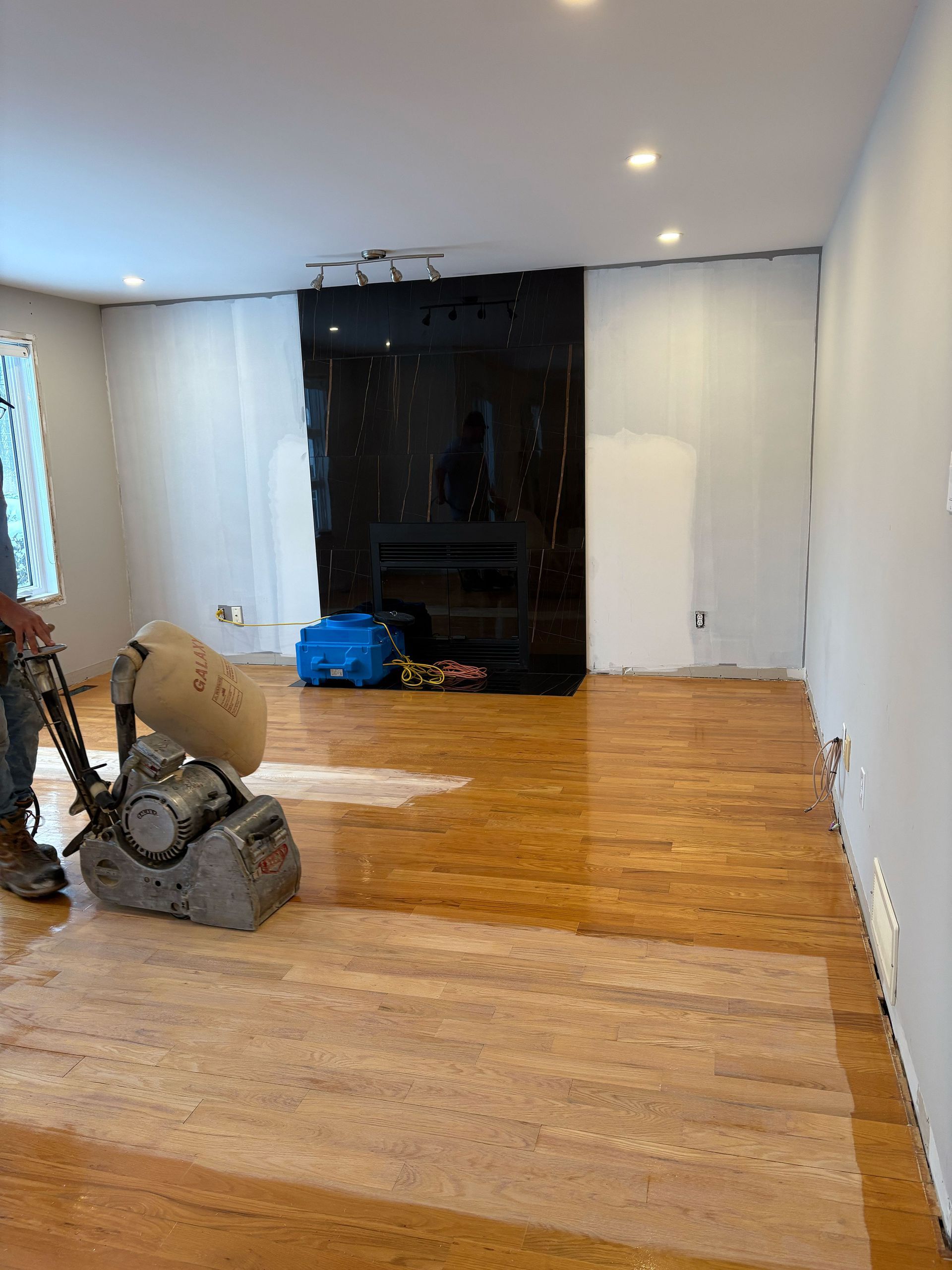 Un homme ponce un parquet dans un salon.