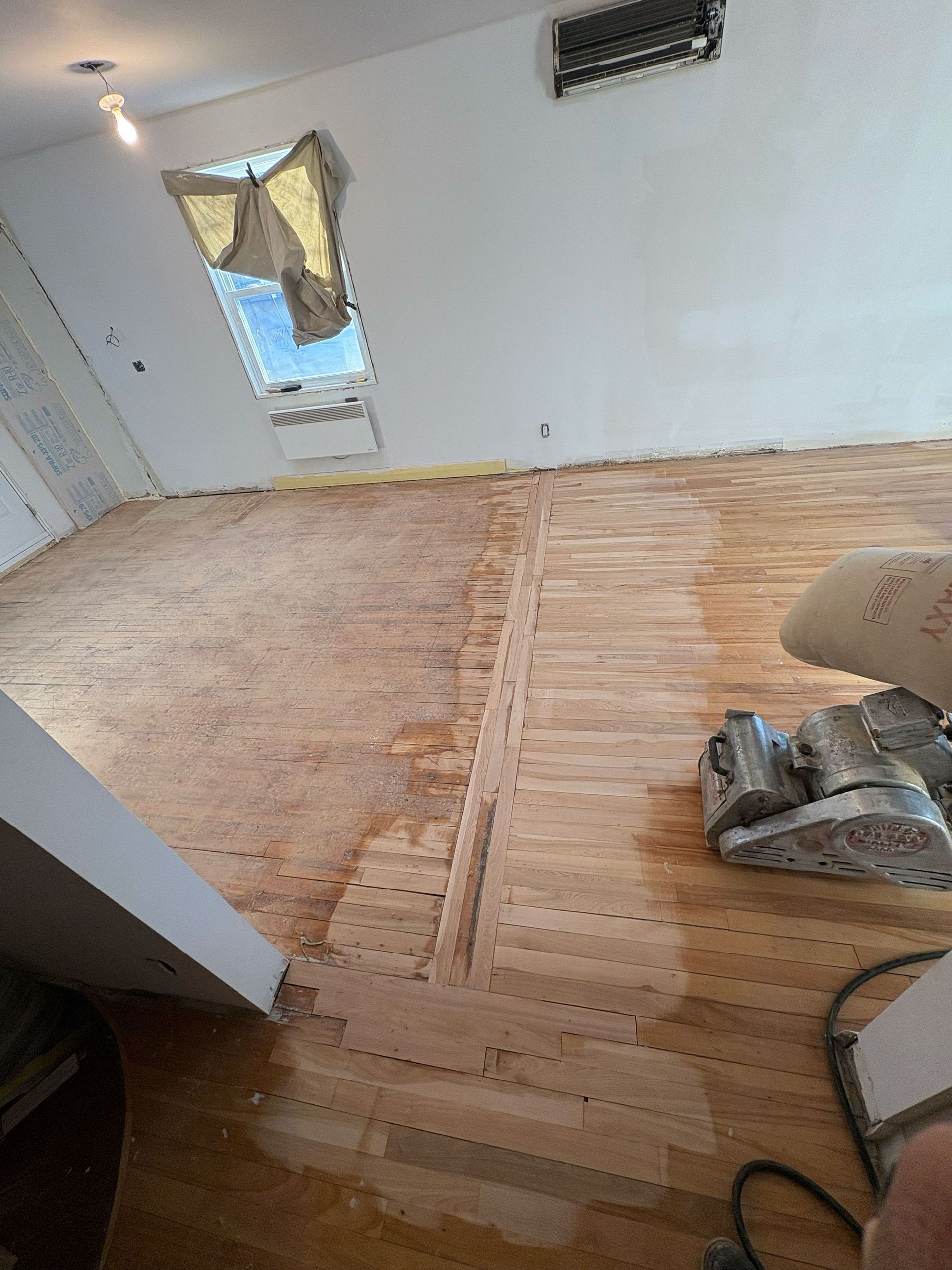 Une personne ponce un plancher en bois avec une machine dans une pièce.